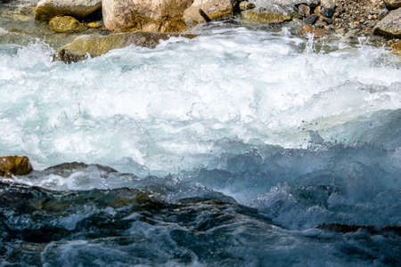 the water of a stormy mountain river flowing among stones and bouldersの写真素材