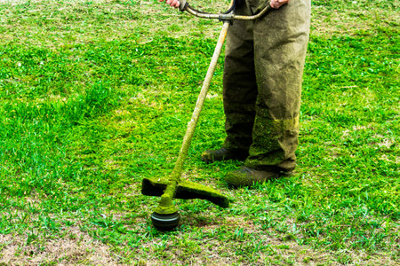man in work clothes mows green grass with trimmer