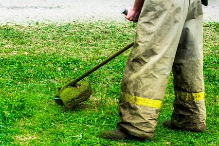 man in work clothes mows green grass with trimmer