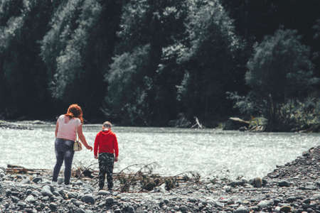 two tourists walk along the banks of a stormy river in the mountainsの写真素材
