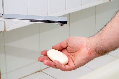a man washes his hands with soap and water under the tap in the bathroom