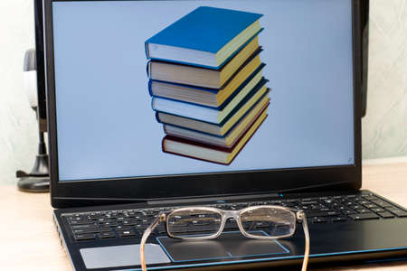 the concept of working at home on the Internet in teaching teaching study education reading glasses lying next to a laptop on the screen of which the image of a stack of books.の写真素材