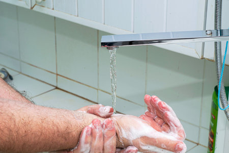 a man washes his hands with soap and water under the tap in the bathroom