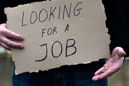 the unemployed person holds in his hand a cardboard tablet with the inscription looking for a job in his other hand the remaining coinsの写真素材