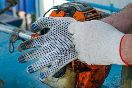 a master in working gloves repairs the engine of an old gas trimmer puts on gloves