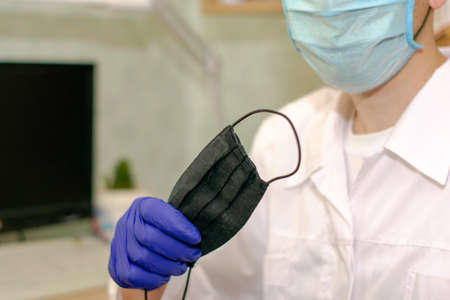 the doctor in the office holds a protective black mask in his handの写真素材