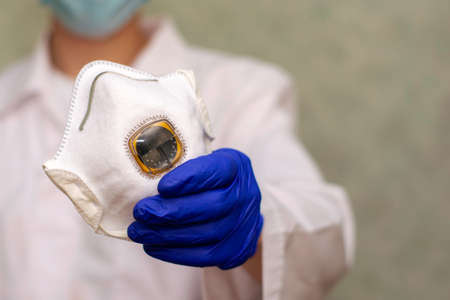 respirator for respiratory protection in the hand of a doctor against the background of a doctor in blurの写真素材