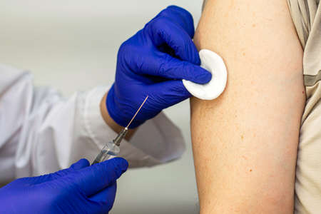 a doctor in blue gloves and a white coat is vaccinated in his hand and wipes the injection siteの写真素材