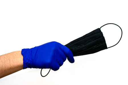 hand in a blue medical glove holds a black hygiene mask on a white backgroundの写真素材