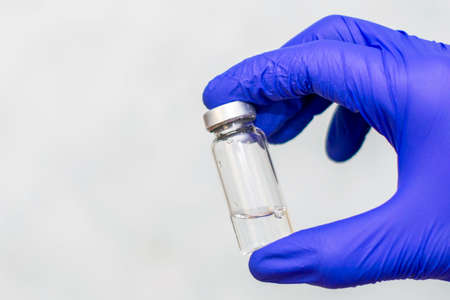 vial with a vaccine in the hands of a doctor in blue protective surgical glovesの写真素材