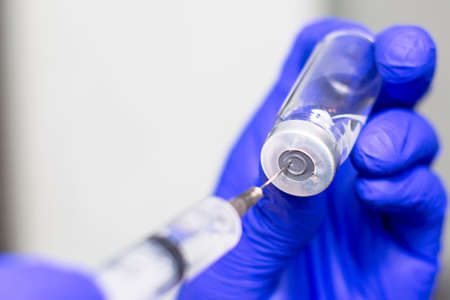 a hand in a blue medical surgical glove picks up a vaccine from an ampoule with a syringeの写真素材