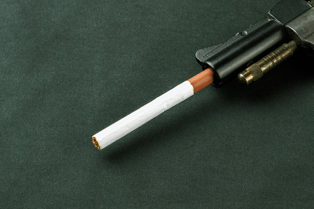 concept of harm to smoking, smoking kills, cigarette sticks out of gun barrel on dark backgroundの写真素材