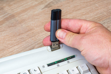 a man's hand inserts a USB flash drive into the connector on the computer keyboard