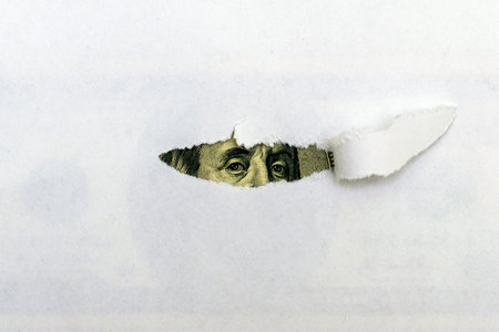 concept from behind a torn sheet of white paper, the eyes of President Franklin peek out from a bill. High quality photoの写真素材