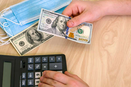 the concept of earning money on a pandemic a person counts money on a calculator there are medical masks nearby. High quality photoの写真素材