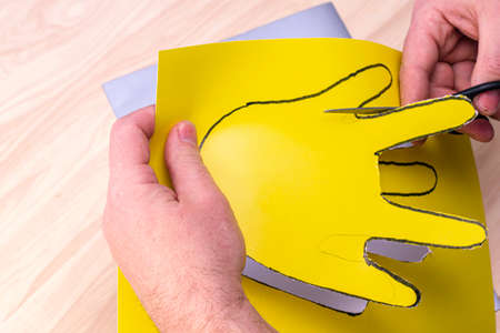 making the simplest Easter bunny with your own hands man with scissors cut out the circled hand on yellow paper. High quality photoの写真素材