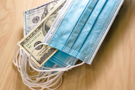 the concept of  business a stack of medical masks lies on the table among the masks are hundred dollar bills. High quality photoの写真素材