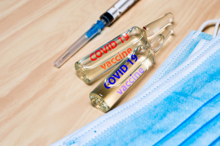 the concept of medicine vaccination. a syringe mask and ampoules with the words vaccine are on the...