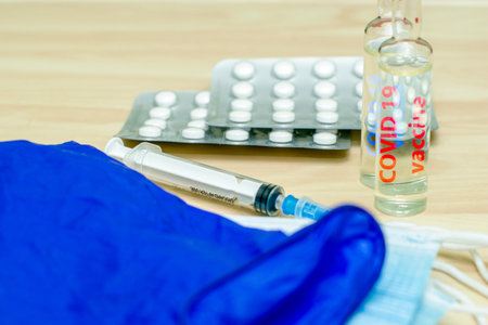 A syringe mask gloves ampoules with the words covid19 vaccine and blisters with pills are on a table