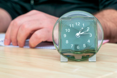 a clock on a table in the background a man working with papers in a blur. High quality photoの写真素材