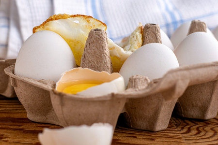 chicken eggs in a cardboard tray one egg is broken the other fried in fried eggs. High quality photoの写真素材