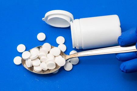 a spoon full of pills and an empty pill jar on a blue background concept medicine a hand in a blue...