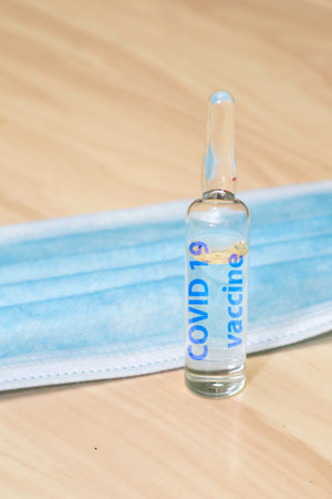 medical hygiene mask and ampoule with medicine on the table the inscription on the ampoule covid 19...