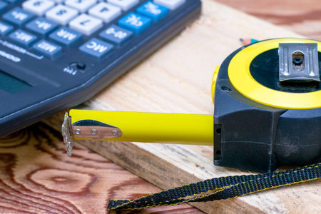 construction meter-tape measure calculator for calculations pencil and wooden board are on the...