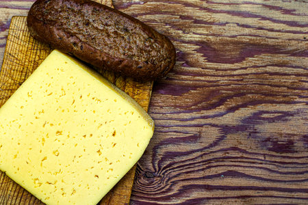 a piece of cheese and one loaf of rye bread on a cutting board copy space. High quality photo