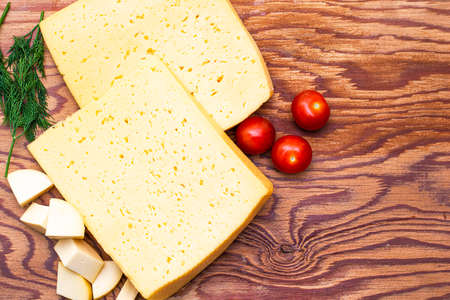 two large pieces of cheese on a wooden table surrounded by tomatoes herbs and small pieces of cheese copyspace. High quality photoの写真素材