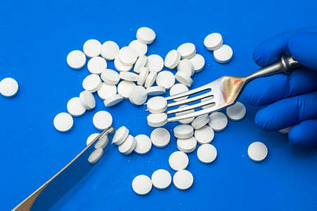 a man wearing blue medical gloves eats pills with a knife and fork. High quality photoの写真素材