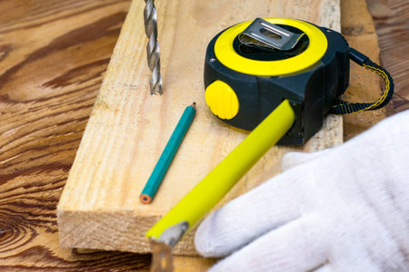 a man with a tape measure measures the distance on the board and drills a hole. High quality photo