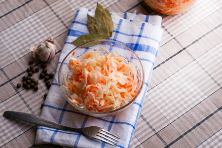 sauerkraut in a glass plate on a napkin on the table a metal fork lies next to garlic sweet peas and bay leaf. High quality photoの写真素材