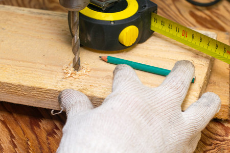 a man drills a board with an electric drill on the board there is a measuring tape and a pencil concept repair construction. High quality photoの写真素材