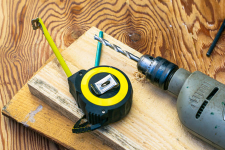 measuring tape pencil and electric drill with drill on board construction repair concept. High...