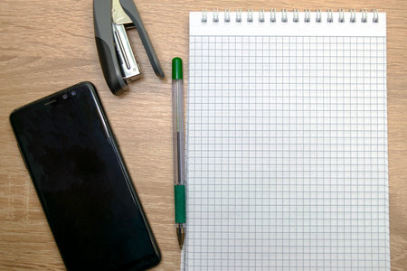 an open notepad for writing a fountain pen a stapler and a smartphone on the table. High quality...