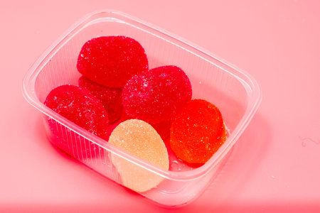 container with colorful marmalade candies on a pink background. High quality photo