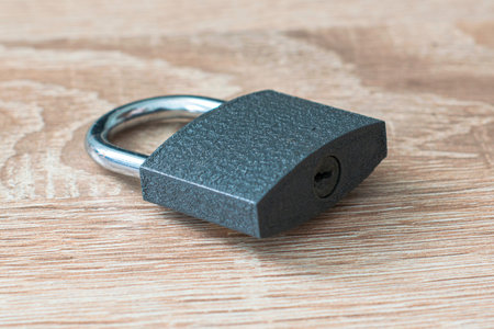 closed iron padlock with a shiny chrome shackle on the wooden surface. High quality photo