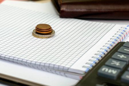 a stack of small coins on an open notepad next to wallet and calculator. High quality photo