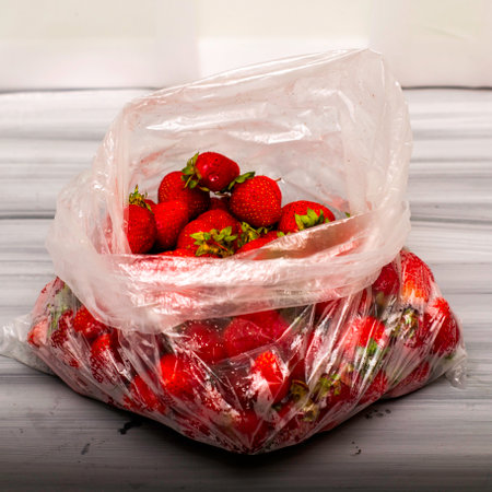 ripe juicy red strawberries in a plastic bag on a wooden table. High quality photoの写真素材