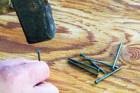 a carpenter hammers a nail into a wooden surface with a hammer. High quality photoの写真素材