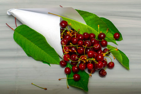 white paper bag with cherries and foliage on a painted wooden surface. High quality photo