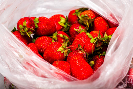 ripe juicy red strawberries in a plastic bag on a wooden table close-up. High quality photoの写真素材