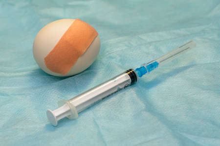 the concept of universal vaccination is a chicken egg with a sticking plaster and a syringe on a medical napkin. High quality photoの写真素材