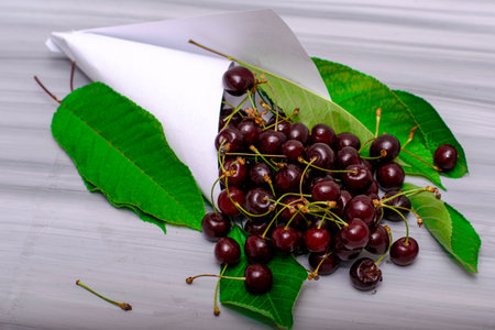 white paper bag with cherries and foliage on a painted wooden surface. High quality photo