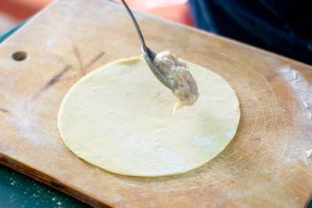 a woman makes Caucasian meat pies-chebureks-on a wooden cutting board, she puts minced meat into the...