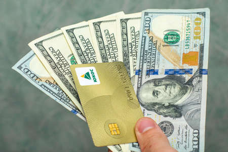 07/29/2021 Divnoye Stavropol Territory Russia the golden refueling card of the YUKOS company and hundred dollar bills in the hands of a person the concept of business raiding oil fuel. High quality photoのeditorial素材