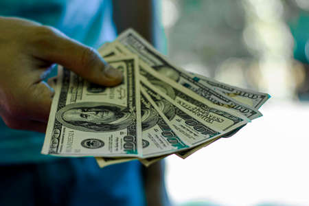 a man holds a stack of hundred-dollar bills in his handの写真素材