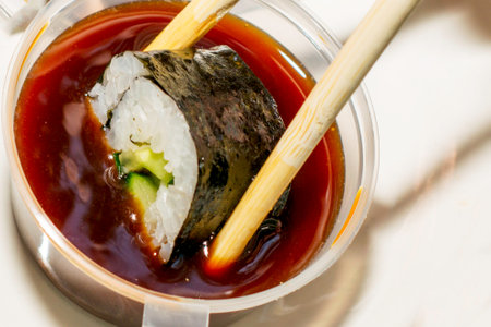 a roll with a cucumber is dipped into a container with soy sauce with wooden sticks close-up. High quality photoの写真素材