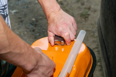 a man holds an orange gasoline canister in his hand next to the car unscrews the cork from the...